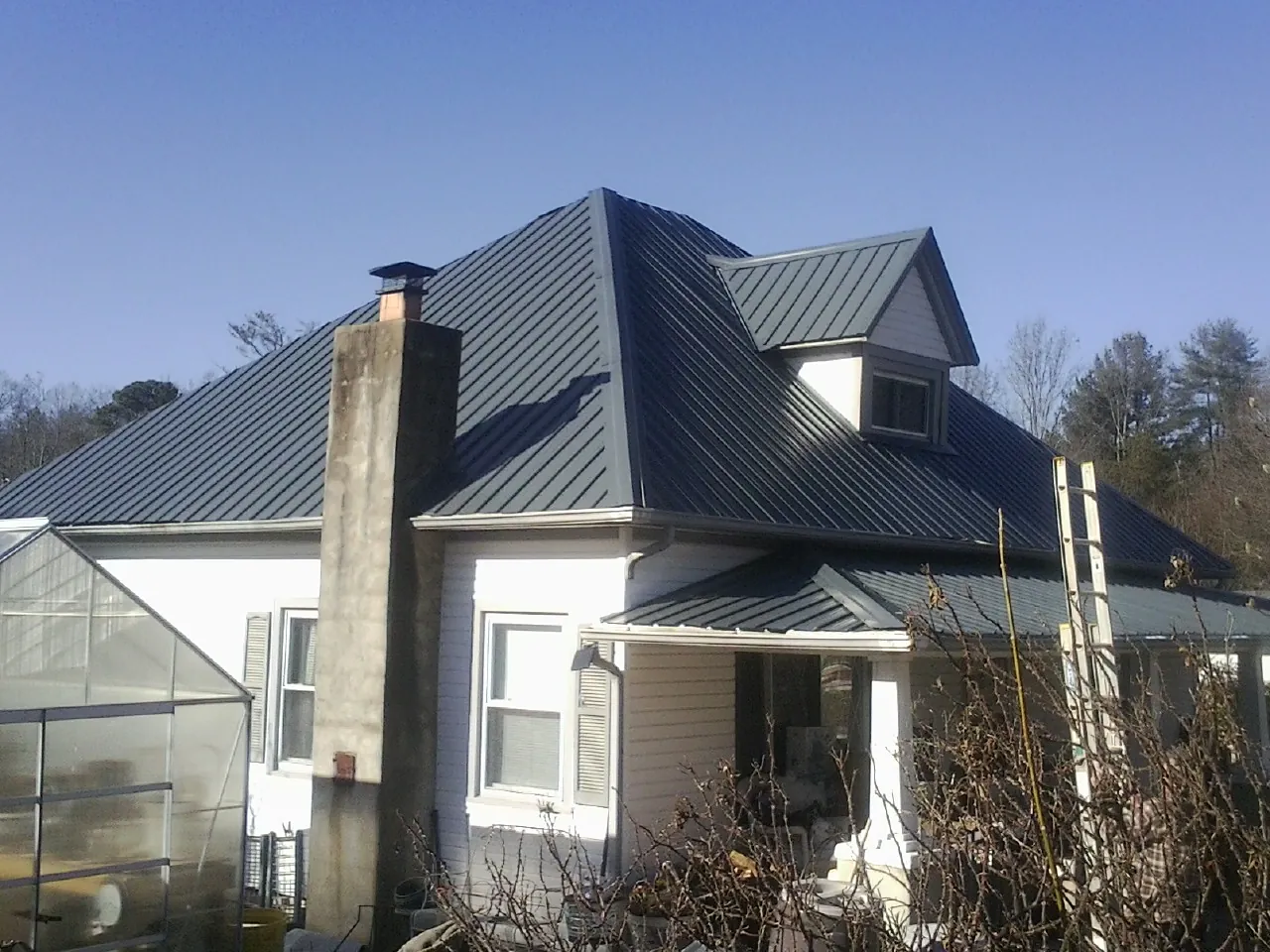 Dark blue standing seam metal roof on a white farmhouse with dormer — Slate & Tile Roof Repair by Roofing Brothers in Gill