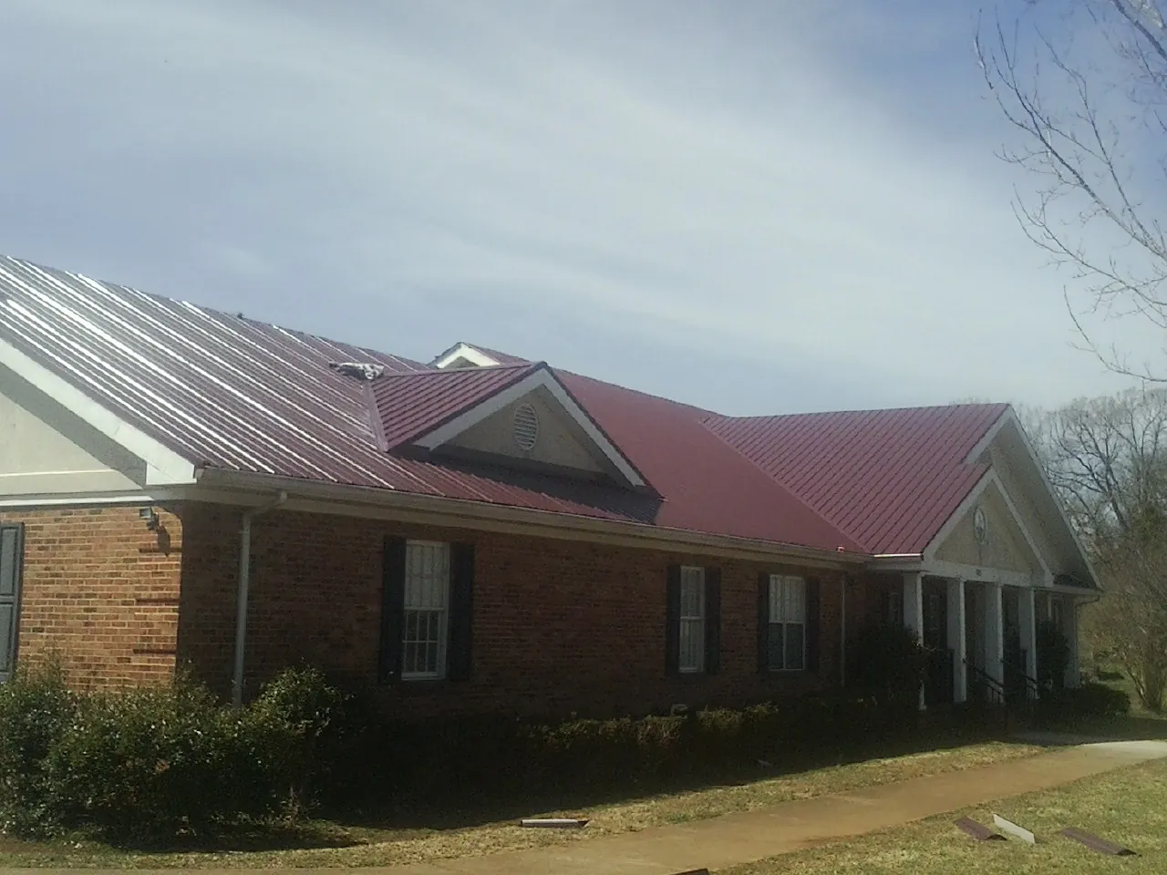 Red metal roof with gabled entries on a long brick building, from a Hail Damage Roof Repair job in Gill