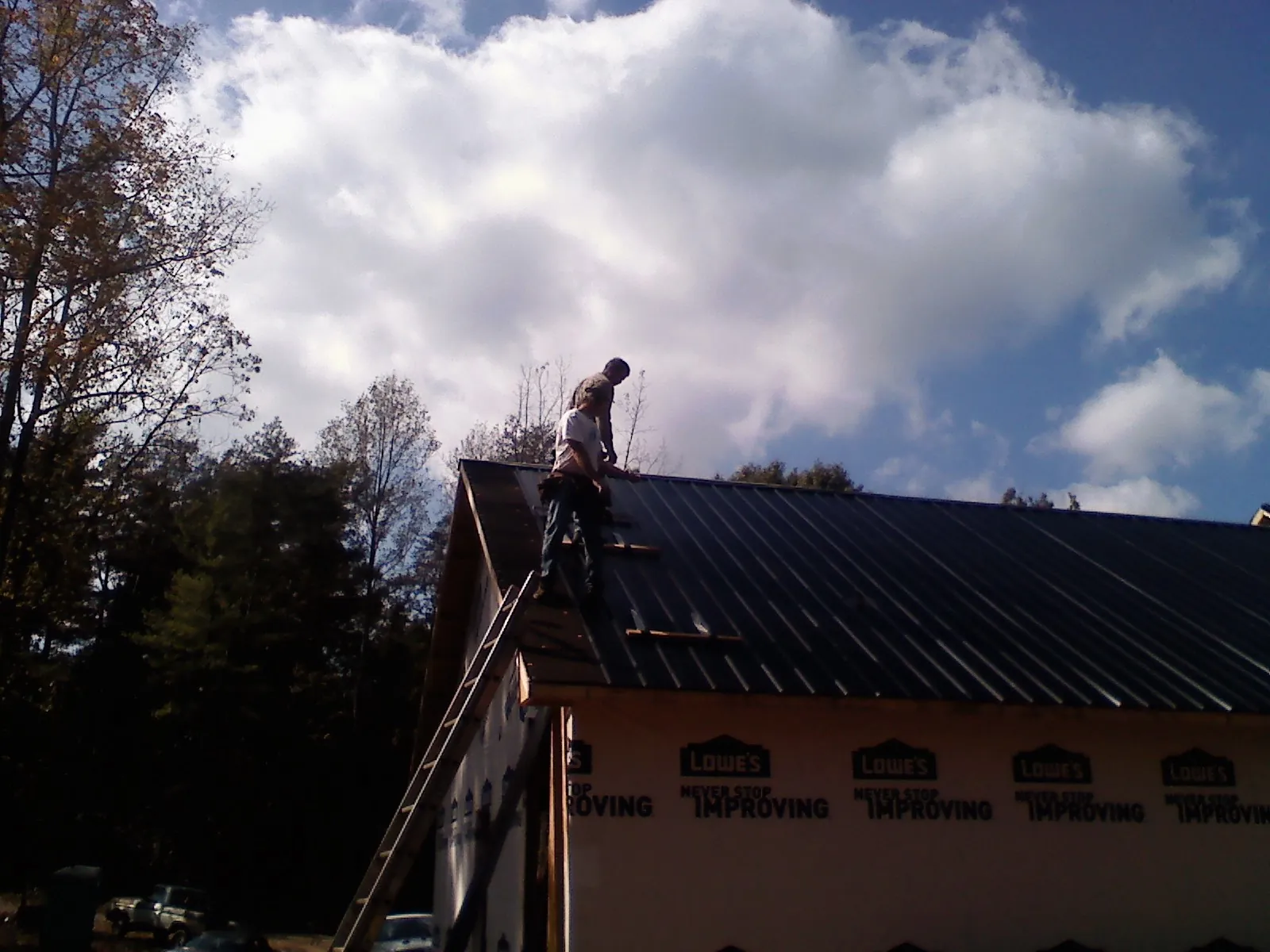 Roofer fastening dark metal panels high against a cloudy sky, from a Roof Inspection job in Gill