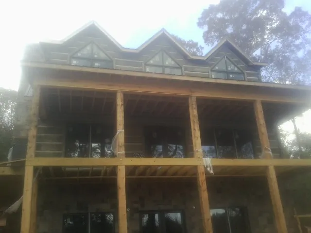 Dormers and porch framing on a large log home under construction — Roof Coating work by our crew in Gill